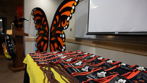 photo of monarch grad stoles displayed on a table and a monarch butterfly arch