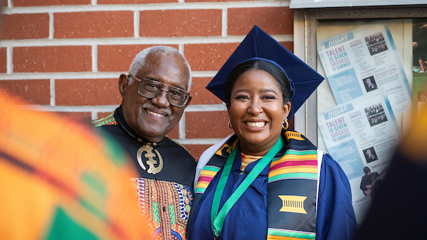 Photo of a graduate posing for a photo with their black grad stole and their family member wearing cultural clothing