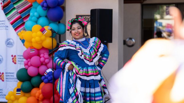 Photo of a Baile Folklorico Dancer posing in cultural clothing in front of an HSI Photo Op with Balloons